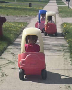 Preschool children riding toy cars on a sunny day at a Becker MN daycare