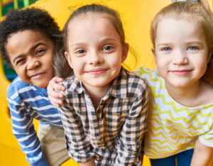 Three preschool children smiling outdoors on a sunny day at a Becker MN daycare
