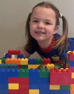 Smiling preschool girl building a block castle in a Becker MN daycare classroom