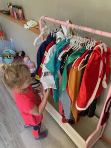 Preschool girl choosing a dress-up outfit from a play clothes rack with costumes