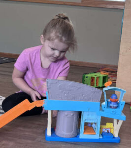 Preschool girl playing with a multi-level toy playset with figures during indoor playtime