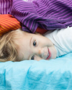 Smiling preschool child resting on a nap mat with colorful blankets at daycare